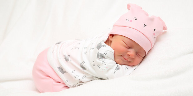 Neugeborenes Baby mit rosafarbener Mütze schläft auf einer weißen Decke.